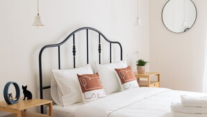 A neatly made bed with white bedding, a black metal headboard, and a bedside table with a lamp and a small potted plant. - Family Apartment | 50m from Acropolis Museum | 2BR 2BA (Athina)