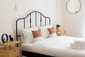 A neatly made bed with white bedding, a black metal headboard, and a bedside table with a lamp and a small potted plant. - Family Apartment | 50m from Acropolis Museum | 2BR 2BA (Athina)