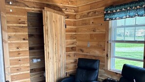 A wooden cabin interior with a wooden ceiling, a window with blinds, and two black leather chairs.