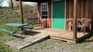 A wooden cabin with a green door, a picnic table, and two benches.