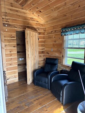 A wooden cabin interior with a wooden ceiling, a window with blinds, and two black leather chairs.