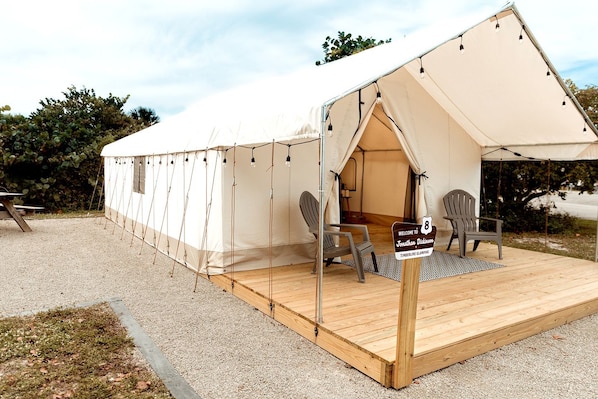 A tented accommodation with a wooden deck, two chairs, and a welcome sign.