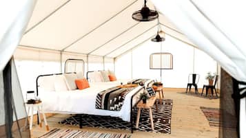 A tent with a bed, a hanging light fixture, and a small table with a sign.