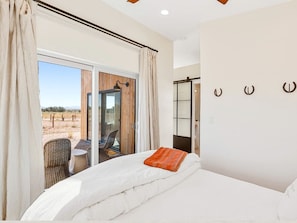 A bedroom with a large bed, a view of the desert through a sliding glass door, a small table with a chair, and a glass door leading to a balcony. - Luxurious Desert Casita with River Rock Shower near Grand Canyon, Arizona (Williams)