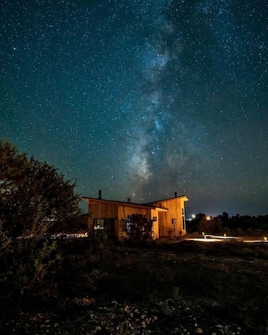 A wooden cabin under a starry night sky with the Milky Way visible.