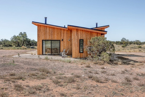 A modern wooden cabin with a large sliding glass door, a small window, and a chair outside.
