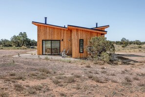 Eine moderne Holzhütte mit einem großen Schiebeglastür, einem kleinen Fenster und einem Stuhl davor.