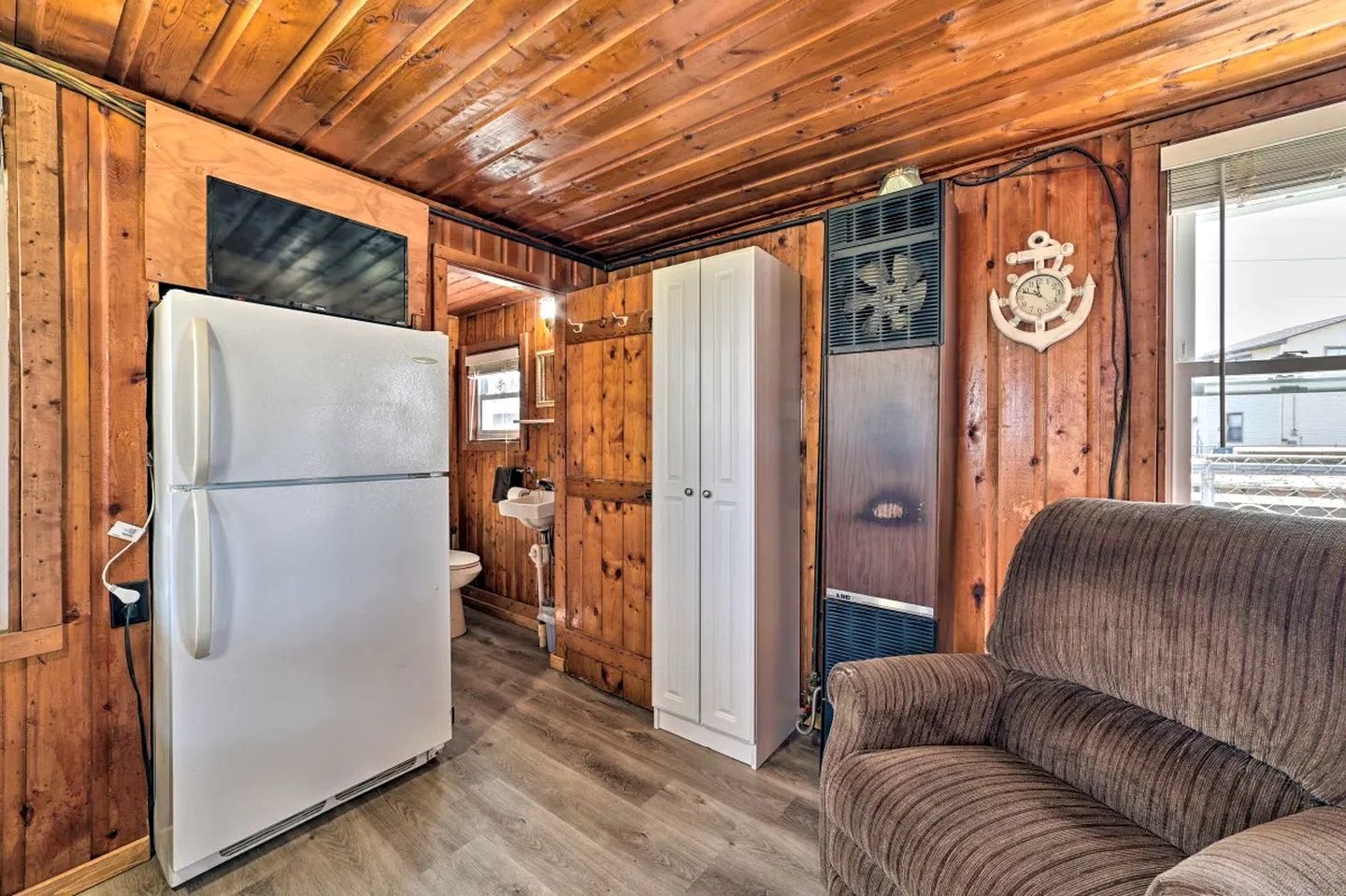 A compact cabin with a wooden interior, a white refrigerator, a sofa, and a bathroom with a sink and toilet.