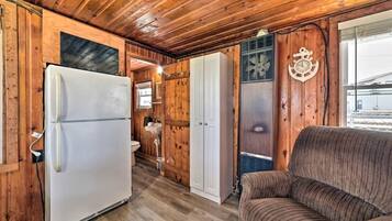 A compact cabin with a wooden interior, a white refrigerator, a sofa, and a bathroom with a sink and toilet.