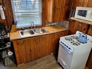 Een kleine keuken met houten kastjes, een spoelbak, een fornuis en een magnetron.