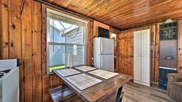 A wooden cabin interior with a kitchen area, including a table with placemats, a refrigerator, and a window.