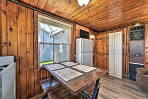 A wooden cabin interior with a kitchen area, including a table with placemats, a refrigerator, and a window. - Lakeside Retreat with Fire Pit & Pet-Friendly Escape in Houghton Lake, Michigan (Houghton Lake)