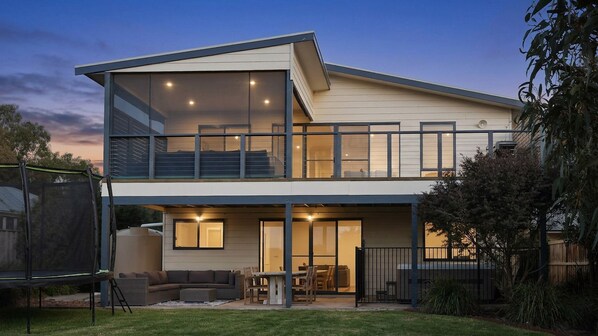 A two-story house with a balcony, a patio with outdoor furniture, and a large window.