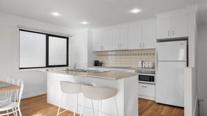 Una cocina moderna con armarios blancos, una isla central con taburetes, horno integrado y refrigerador.