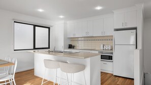 A modern kitchen with white cabinetry, a central island with stools, a built-in oven, and a refrigerator.