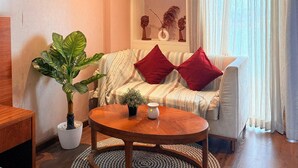 Ein Wohnzimmer mit einer Couch, einem runden Holztisch, einem Blumentopf und einem an der Wand hängenden Bild.