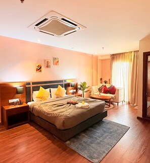 Quarto de hotel com cama, mesas de cabeceira, escrivaninha, cadeira e janela com cortinas.
