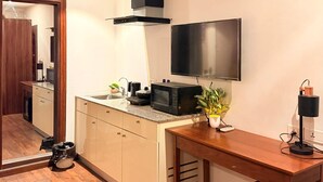 Eine kompakte Küche mit Mikrowelle, einem kleinen Tisch, einem an der Wand befestigten Fernseher und einer sichtbaren Tür zu einem anderen Raum.