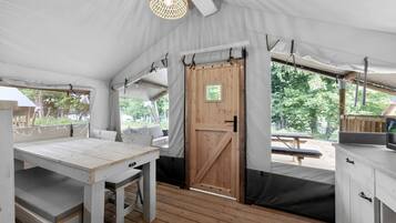 A tent with a wooden table, bench seating, a door, and a view of the outdoors.