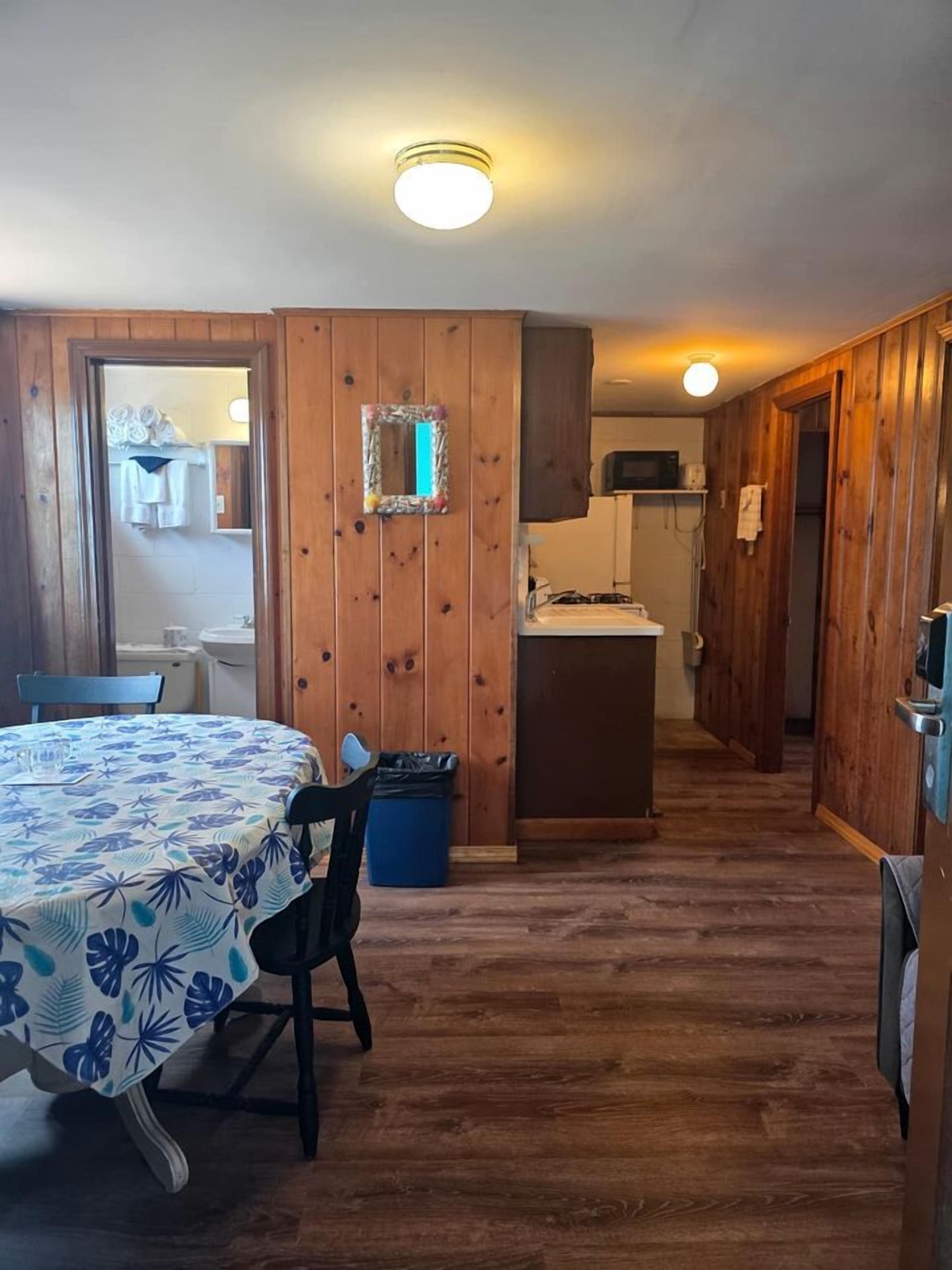 Una habitación con mesa de comedor, sillas, una pequeña cocina y paredes de madera.