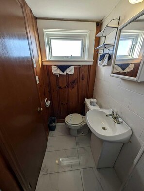 A compact bathroom with a toilet, sink, and window. - Elegant Oceanfront Cottages with Private Beach Access in North Truro, Massachusetts (North Truro)