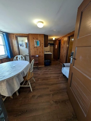 Ein Zimmer mit Holzboden, einem Esstisch mit Stühlen, einem Bett und einer Tür.