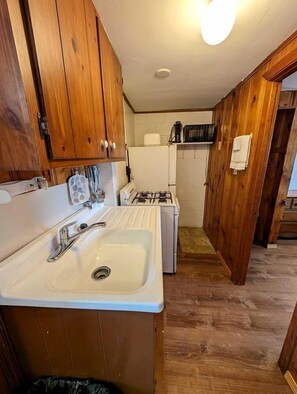 Une cuisine de taille réduite, dotée de meubles en bois, d’un évier, d’un four à micro-ondes et d’une cuisinière.