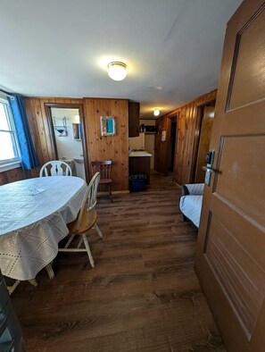 A room with a wooden floor, a dining table with chairs, a bed, and a door. - Elegant Oceanfront Cottages with Private Beach Access in North Truro, Massachusetts (North Truro)