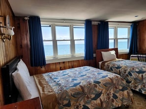Ein Zimmer mit zwei Betten, Holzwänden, einem Fenster mit Vorhängen und Meerblick.