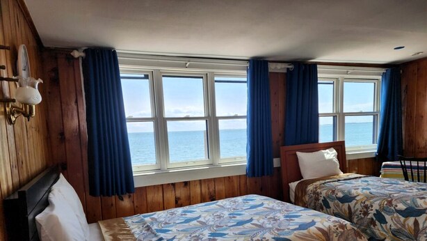Ein Zimmer mit zwei Betten, Holzwänden, einem Fenster mit Vorhängen und Meerblick.