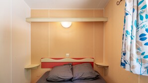 Una habitación pequeña con cama individual, cabecera roja, mesitas de noche y una lámpara fijada a la pared.