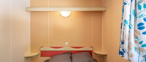 A small, single-bed room with a red headboard, bedside tables, and a wall-mounted light fixture.