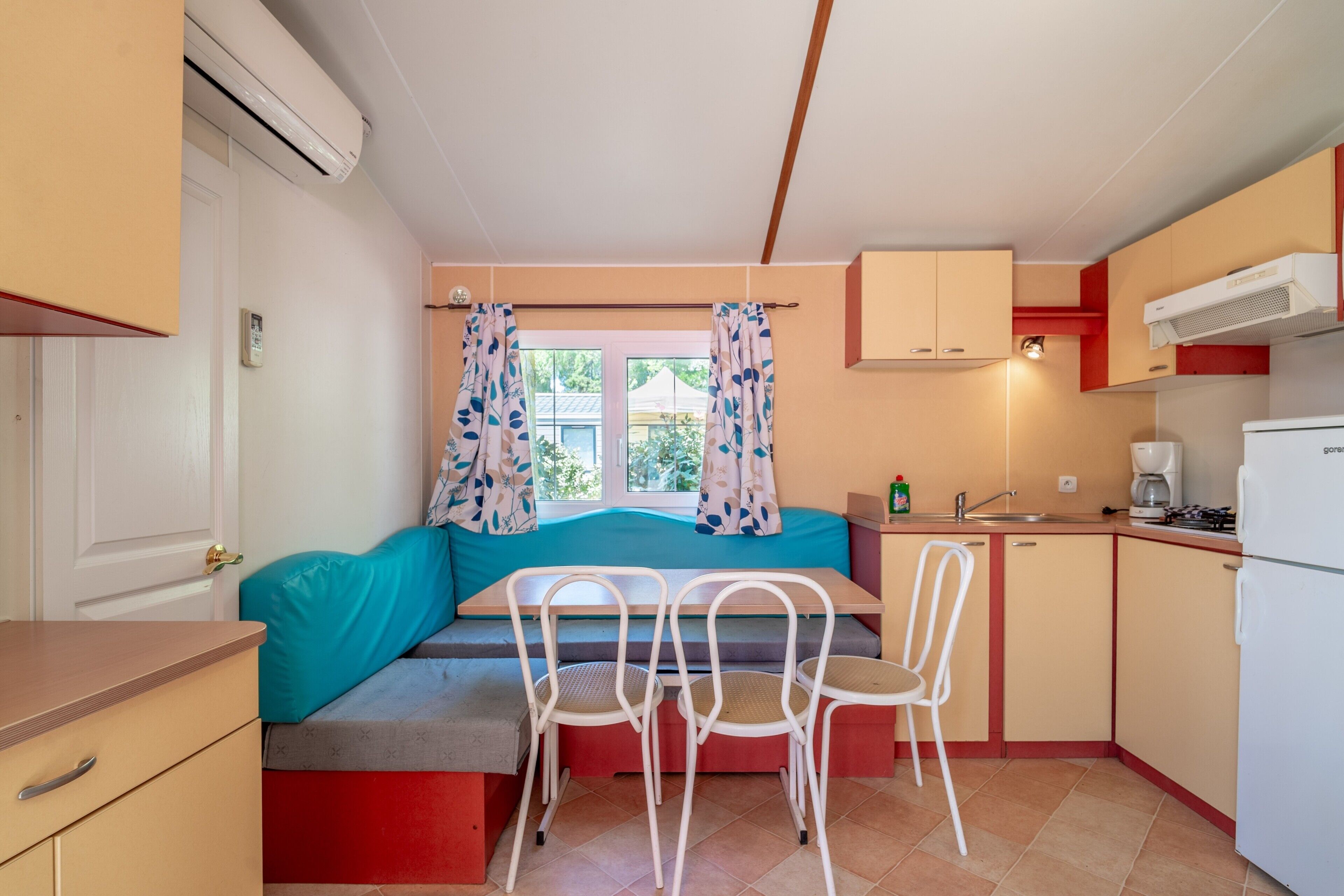 A compact kitchen with a dining area, a built-in bench, and a window with curtains.
