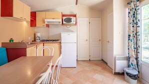 Cocina compacta con microondas, estufa y refrigerador. Hay una mesa de comedor con sillas y una ventana con cortinas.