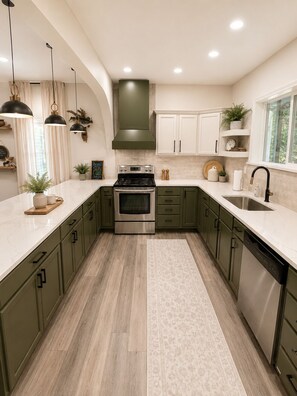 A kitchen with a central island, stainless steel appliances, and green cabinetry.