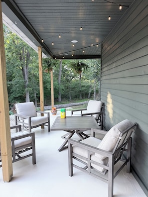 An outdoor patio with a wooden table and chairs, surrounded by greenery.