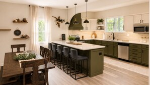 A modern kitchen with a central island, dark green cabinets, and a white countertop.