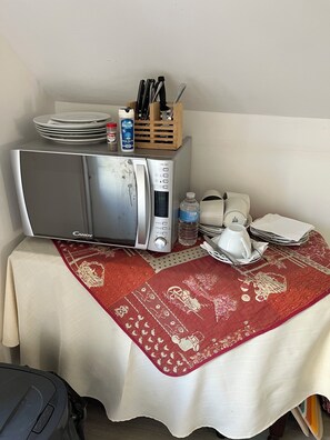 A microwave on a table with plates, a bottle, and a cup.