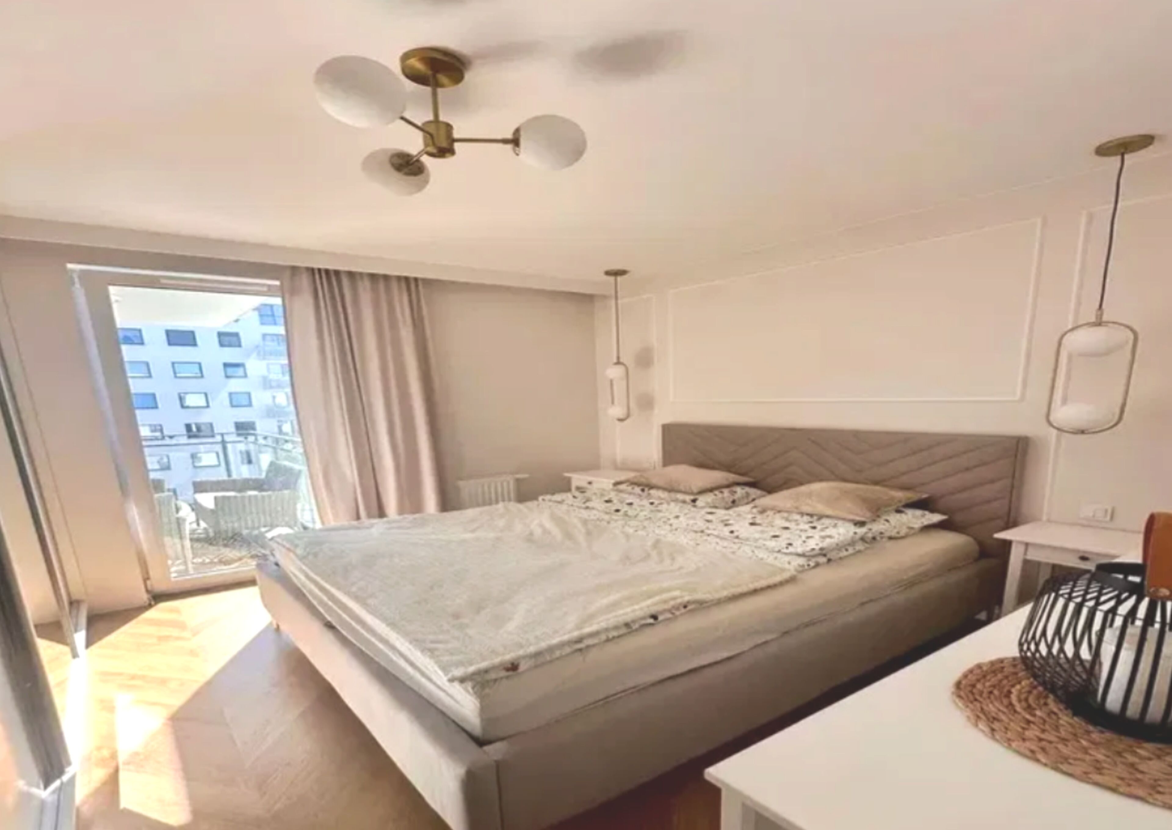 A bedroom with a bed, a bedside table, a lamp, a ceiling fan, and a view of the outside.