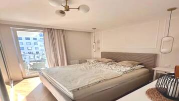 A bedroom with a bed, a bedside table, a lamp, a ceiling fan, and a view of the outside.