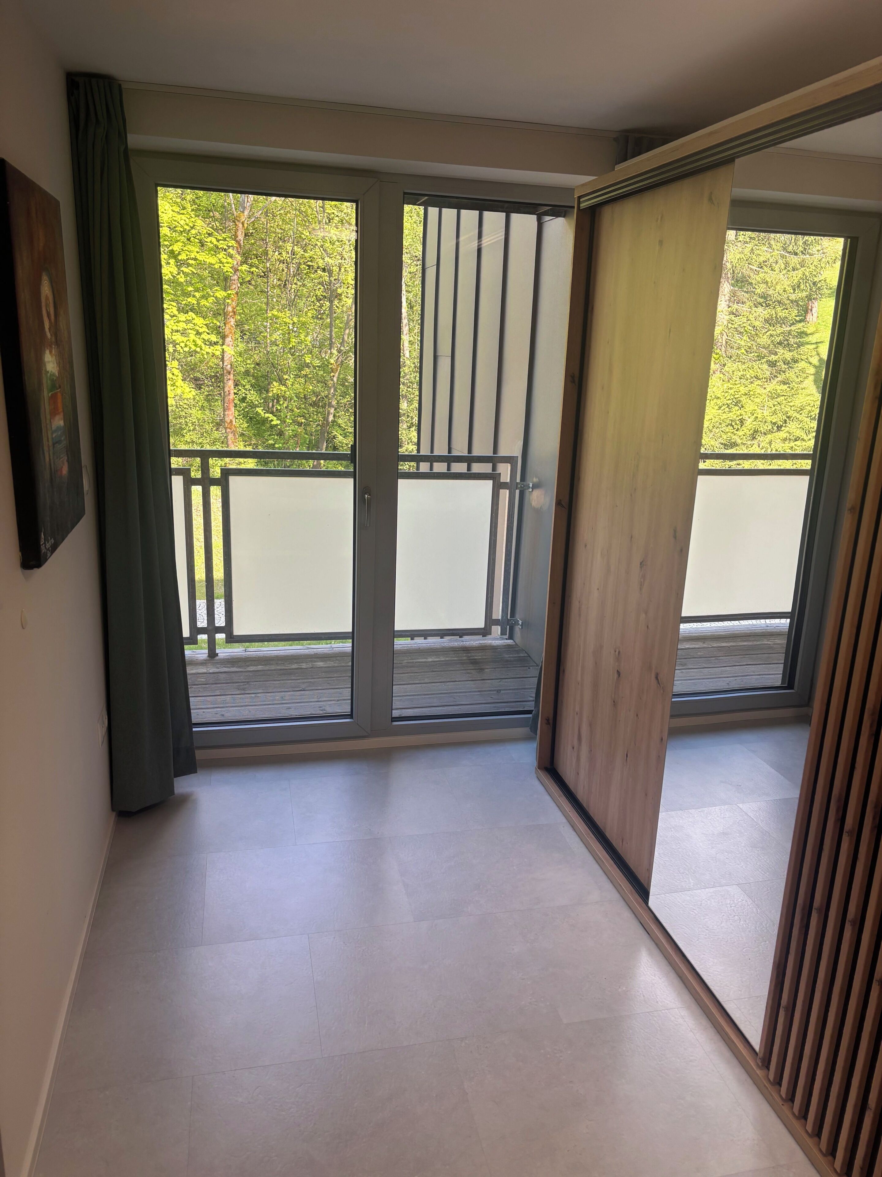 Ein Zimmer mit einer großen Schiebetür, die auf einen Balkon mit Blick auf Bäume führt.