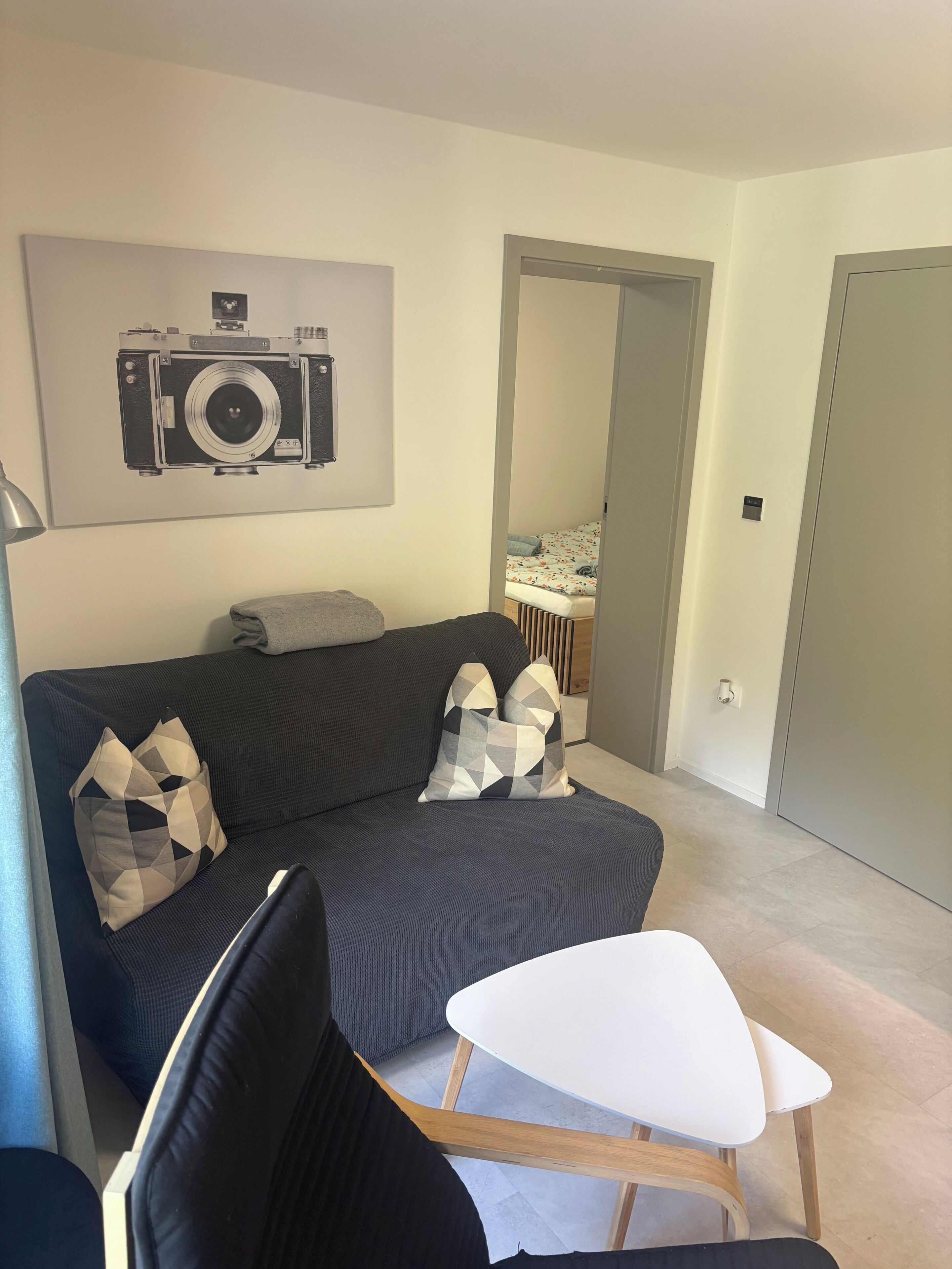 Ein Wohnzimmer mit einem dunklen Sofa, einem weißen Tisch und einer Kamera an der Wand.