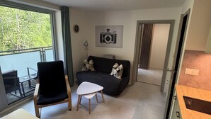 A modern living room with a sofa, a chair, a small table, and a kitchen area with cabinets.