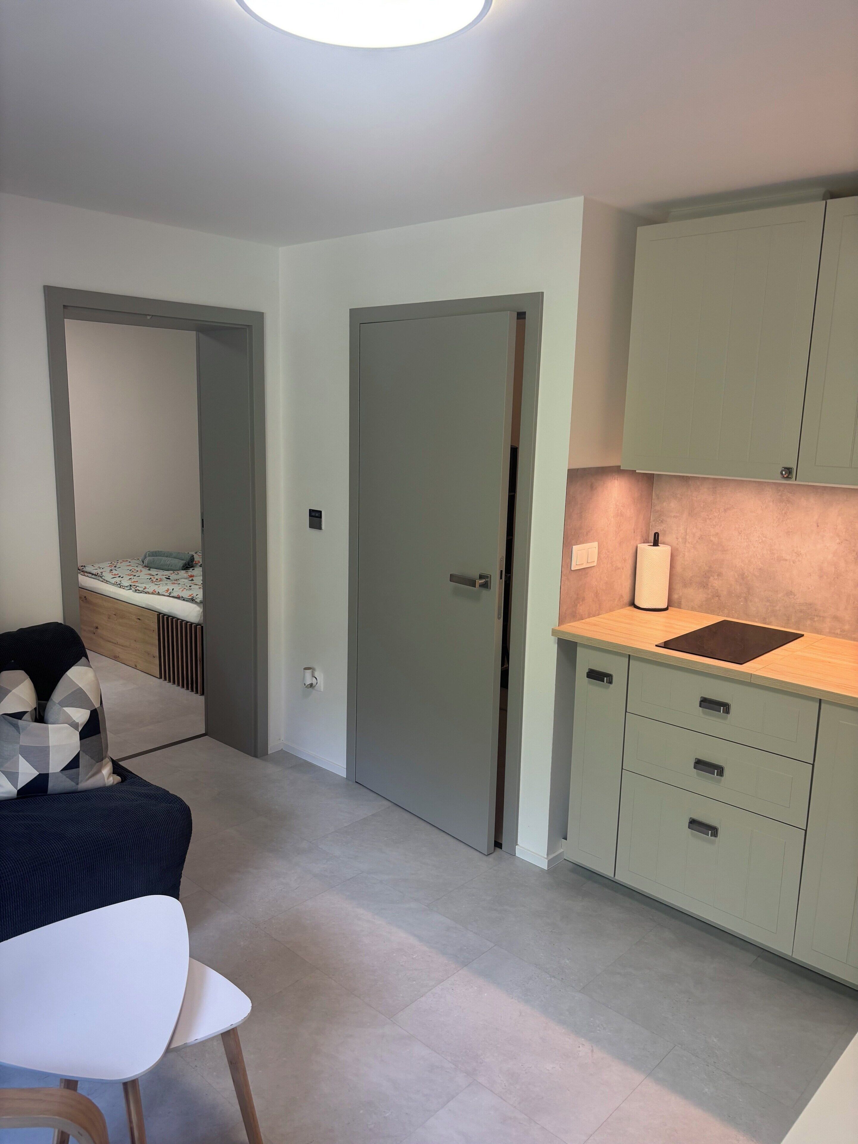 Une chambre moderne avec un lit, une chaise et un bureau. Une porte donne accès à une autre pièce.
