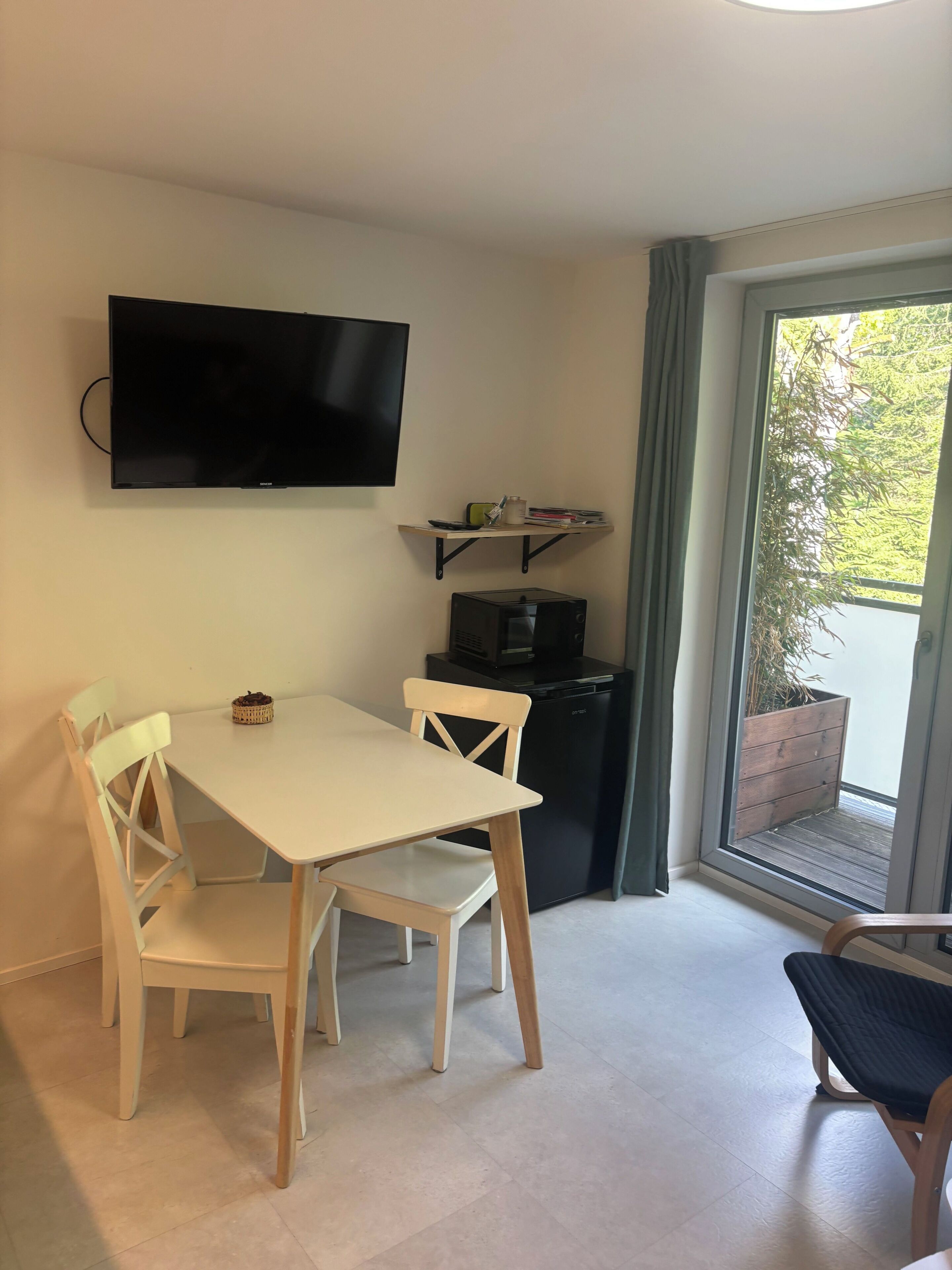Habitació amb televisió de pantalla plana penjada a la paret, taula petita amb cadires, microones i porta corredissa de vidre que dona a zona exterior.