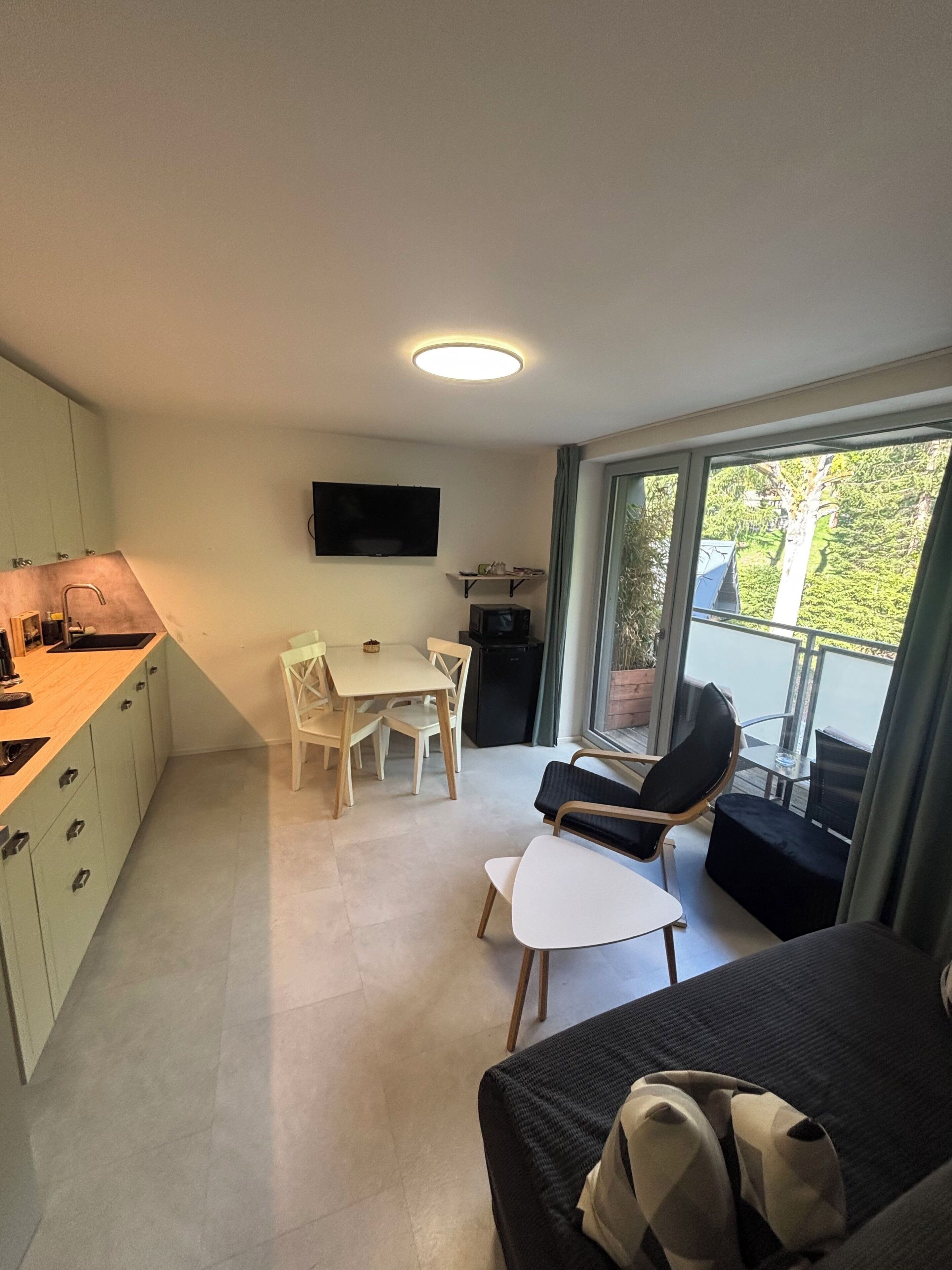 A modern kitchen with a dining area, a flat-screen TV, and a balcony with a view.