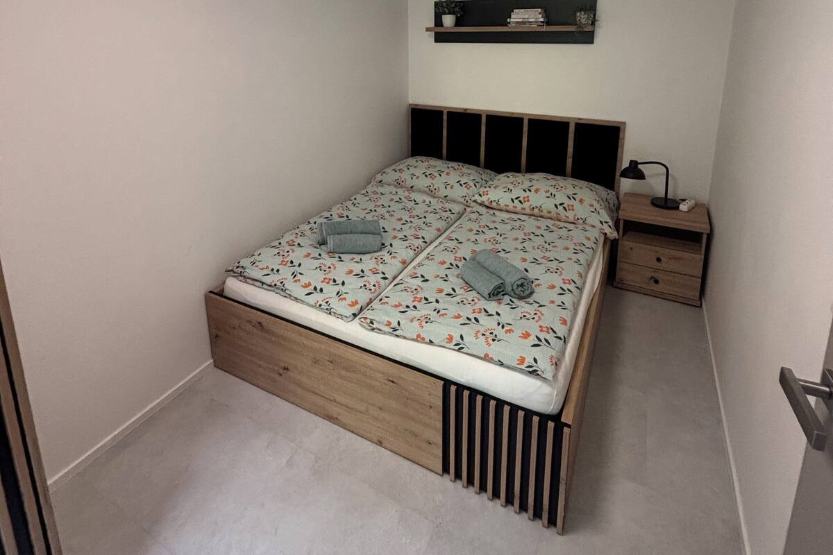 Un dormitorio con cama, mesita de noche, estante en la pared y una lámpara de techo.