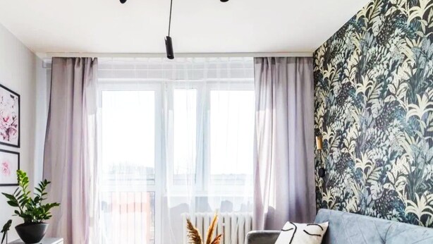 A modern living room with a grey sofa, a black coffee table, a patterned wall, and a large window with sheer curtains.