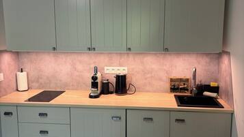 Eine Küche mit hellgrünen Schränken, einer Holz Arbeitsplatte, einer Spüle, einer Kaffeemaschine und einem weißen Stuhl.
