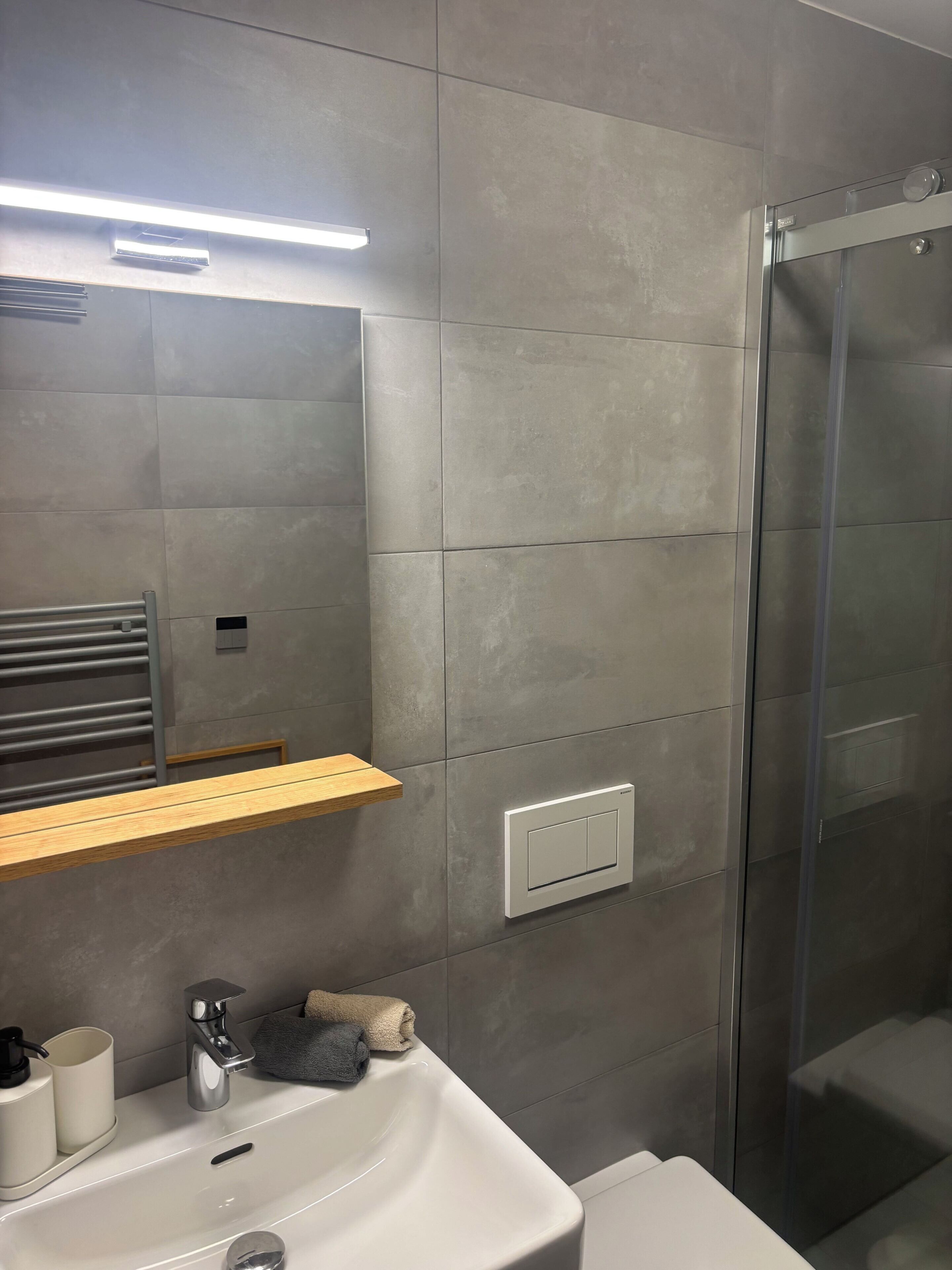 Ein modernes Badezimmer mit Waschbecken, Spiegel, Handtuchhalter, Duschkabine und einer Leuchte.